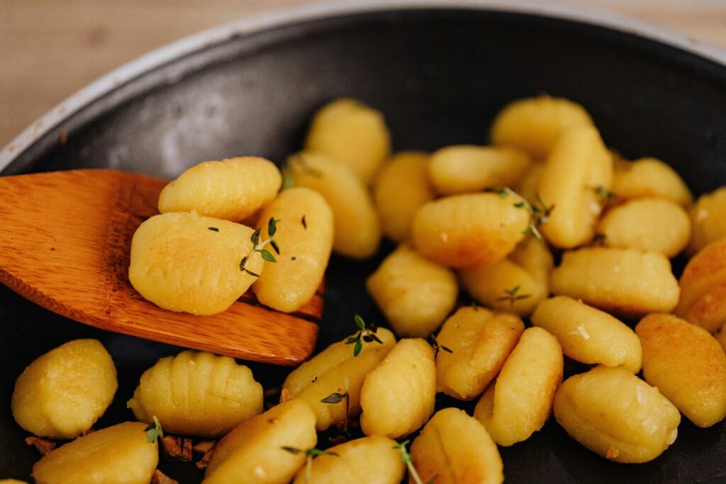 Golden gnocchi with herbs being cooked and served with a wooden spatula.
