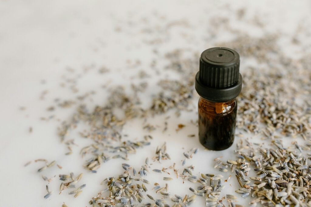 Close-up of a brown glass bottle of lavender essential oil surrounded by dried lavender flowers.