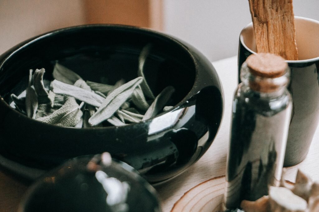 A close-up of sage leaves in a ceramic bowl with aromatic bottles, evoking a natural, tranquil setting.