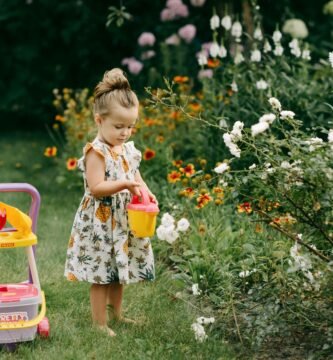 A young girl waters flowers in a garden with a toy watering can, surrounded by vibrant blooms.