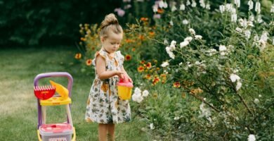 A young girl waters flowers in a garden with a toy watering can, surrounded by vibrant blooms.